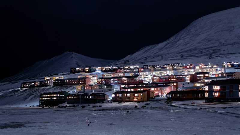 Houses of Longyearbyen lit at night below snowy hills